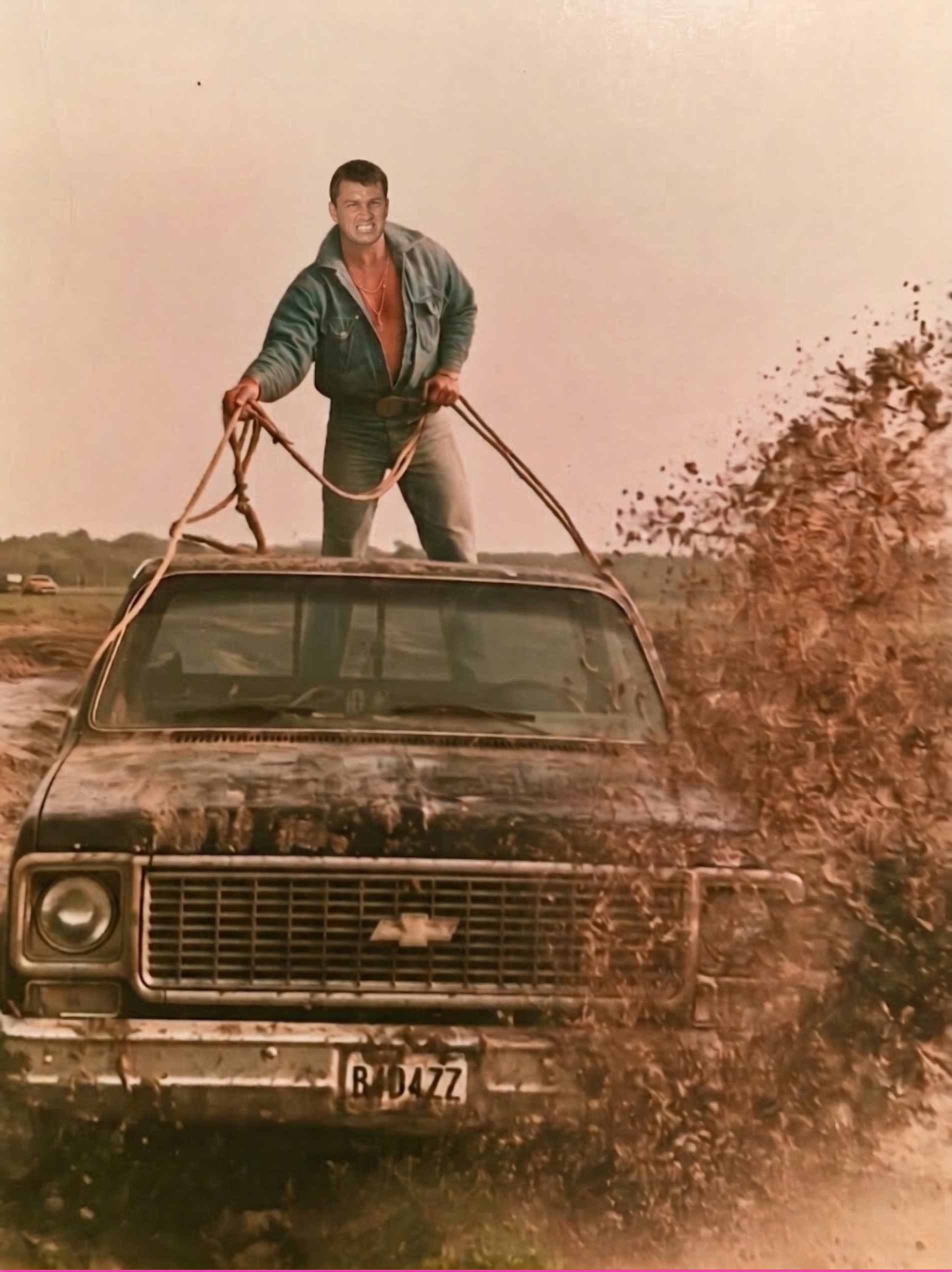 Steven Burns standing atop a mud-covered black Chevrolet pickup, gripping ropes like reins as mud sprays across a field.